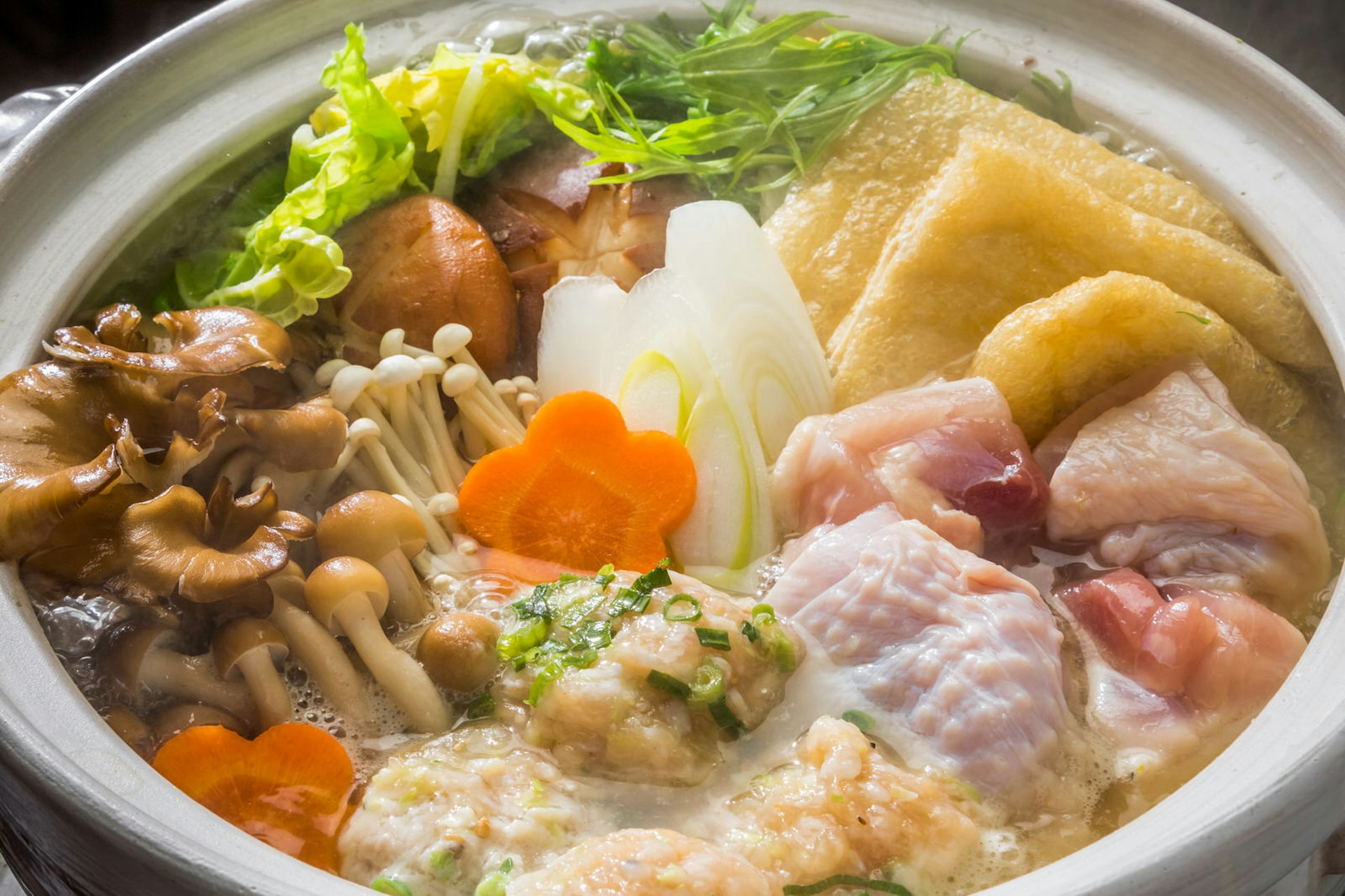 Close up of a hotpot bowl of broth, chicken and various vegetables
