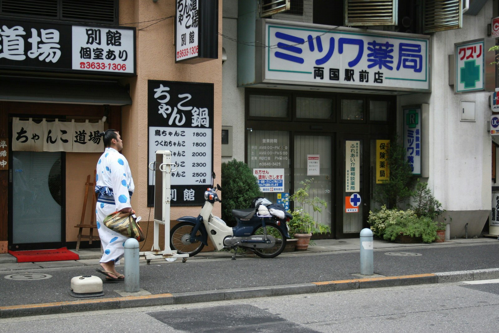 A sumo wrestler dressed in cotton kimono walks past a chanko nabe restaurant on a Tokyo street