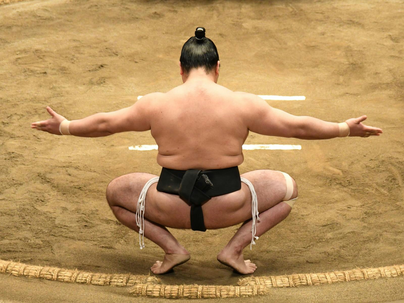 View of the back of a sumo wrestler squatting in the sumo ring with arms outstretched