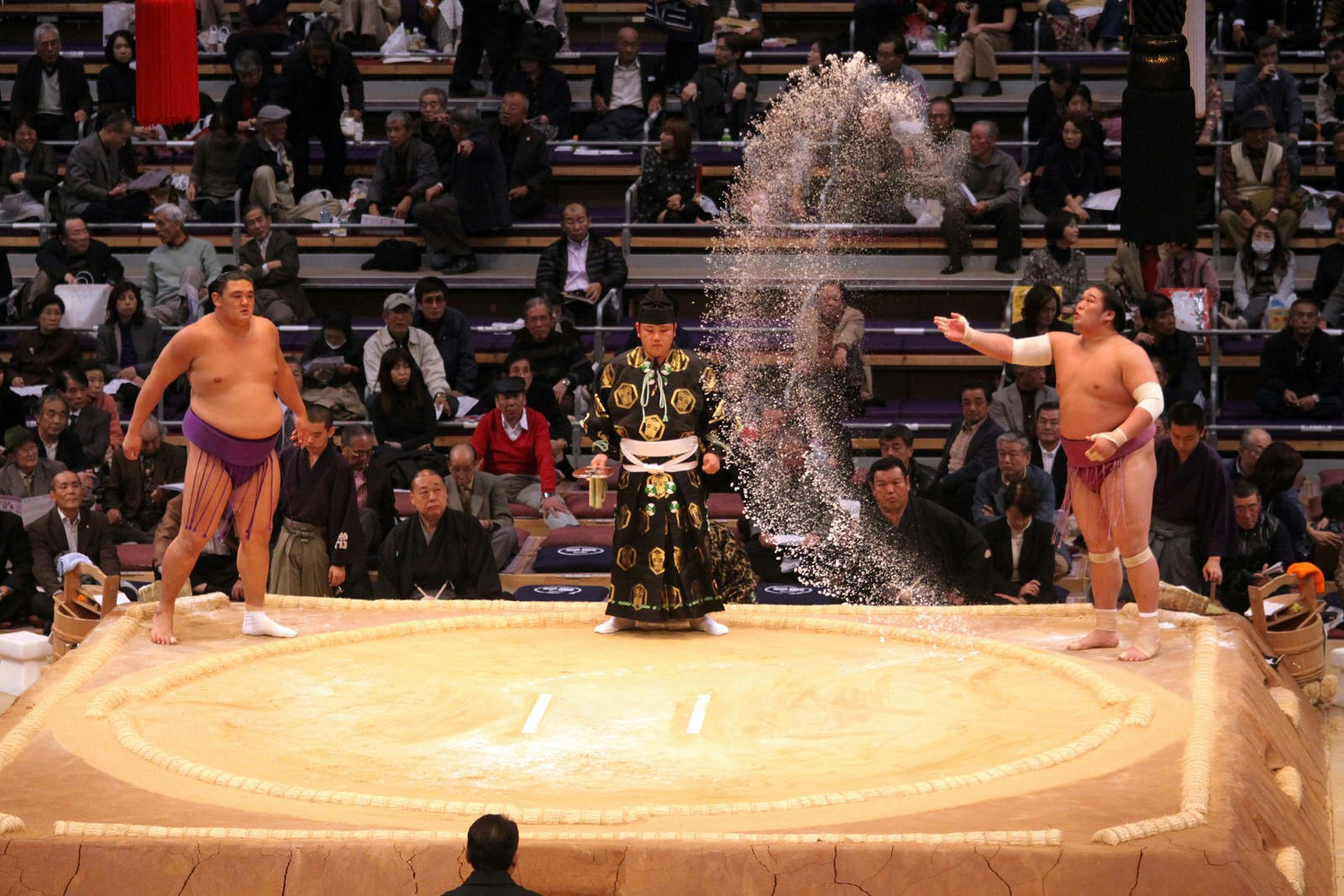 A sumo wrestler throws a large handful of salt across the sumo ring