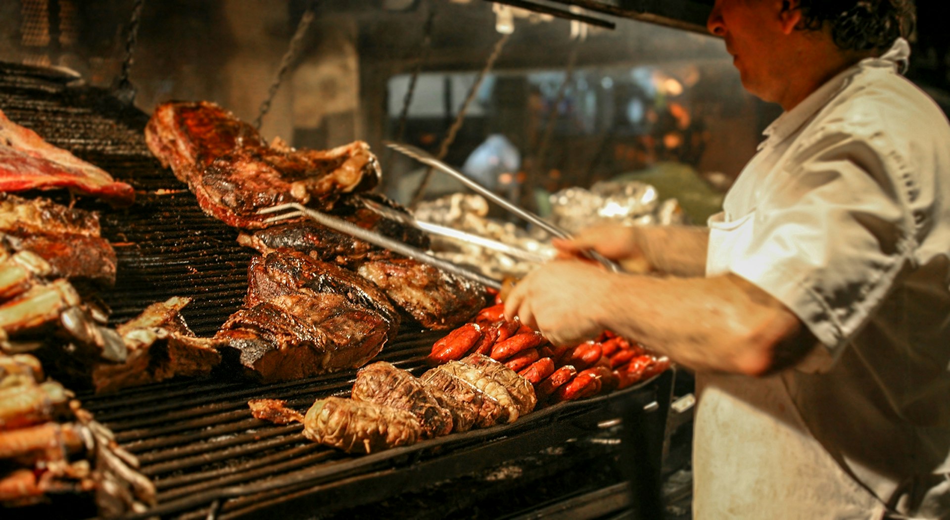 A chef grills large hunks of meat on an iron grill in Argentina