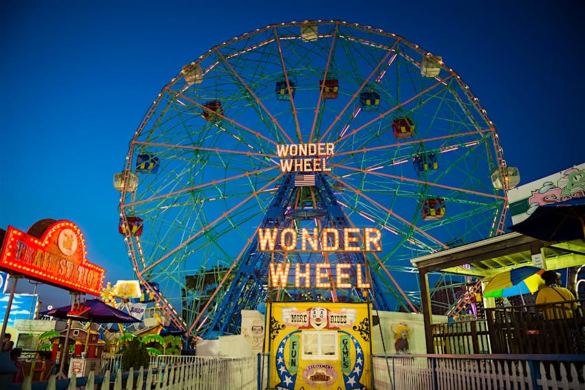 The wonder wheel Ferris Wheel is lit up over Coney Island amusement park in New York at night; ways to enjoy New York City in the summer