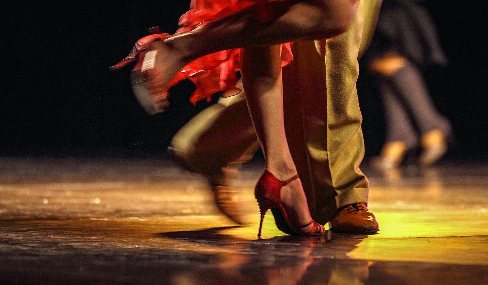 A close up of tango dancers' feet while dancing on a dark stage