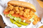 Shrimp po' boy sandwich on white paper with two pickles © kcline / Getty Images