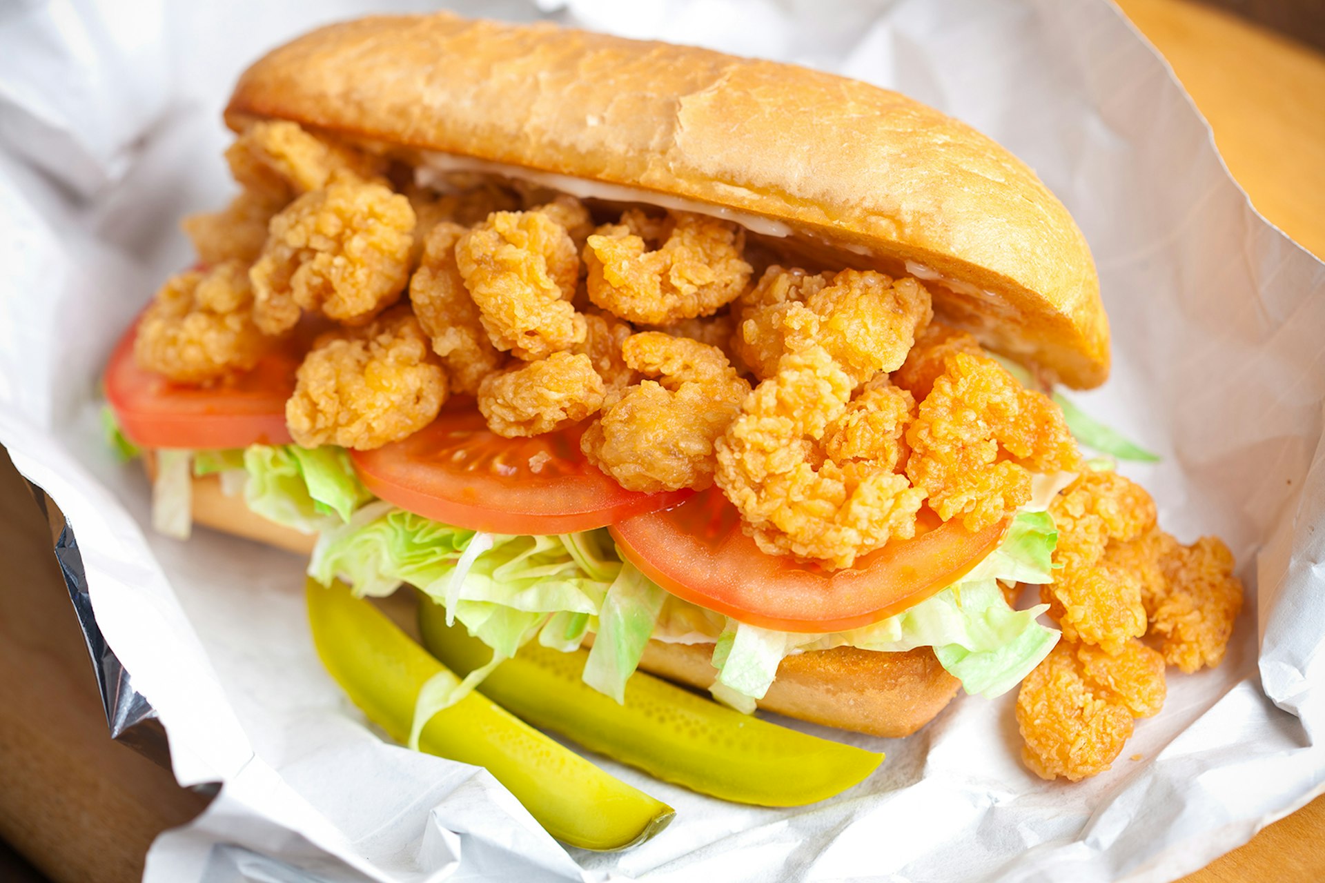 Shrimp po' boy sandwich on white paper with two pickles © kcline / Getty Images