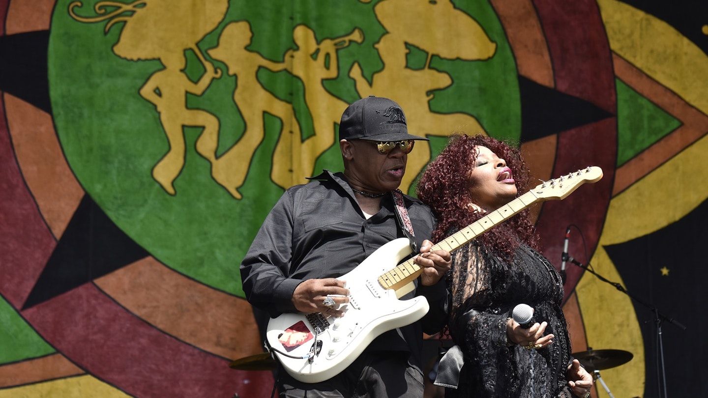 Disco legend Chaka Khan leans back against a man playing the electric guitar as she sings in front of a large tapestry; New Orleans Festivals