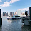 The NYC ferry floats in the harbor near Queens with skyscrapers in the background on a sunny fall day