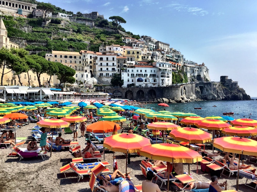 Beachgoers relaxing under umbrellas on the Amalfi Coast. Image by Mark Waind / EyeEm / Getty
