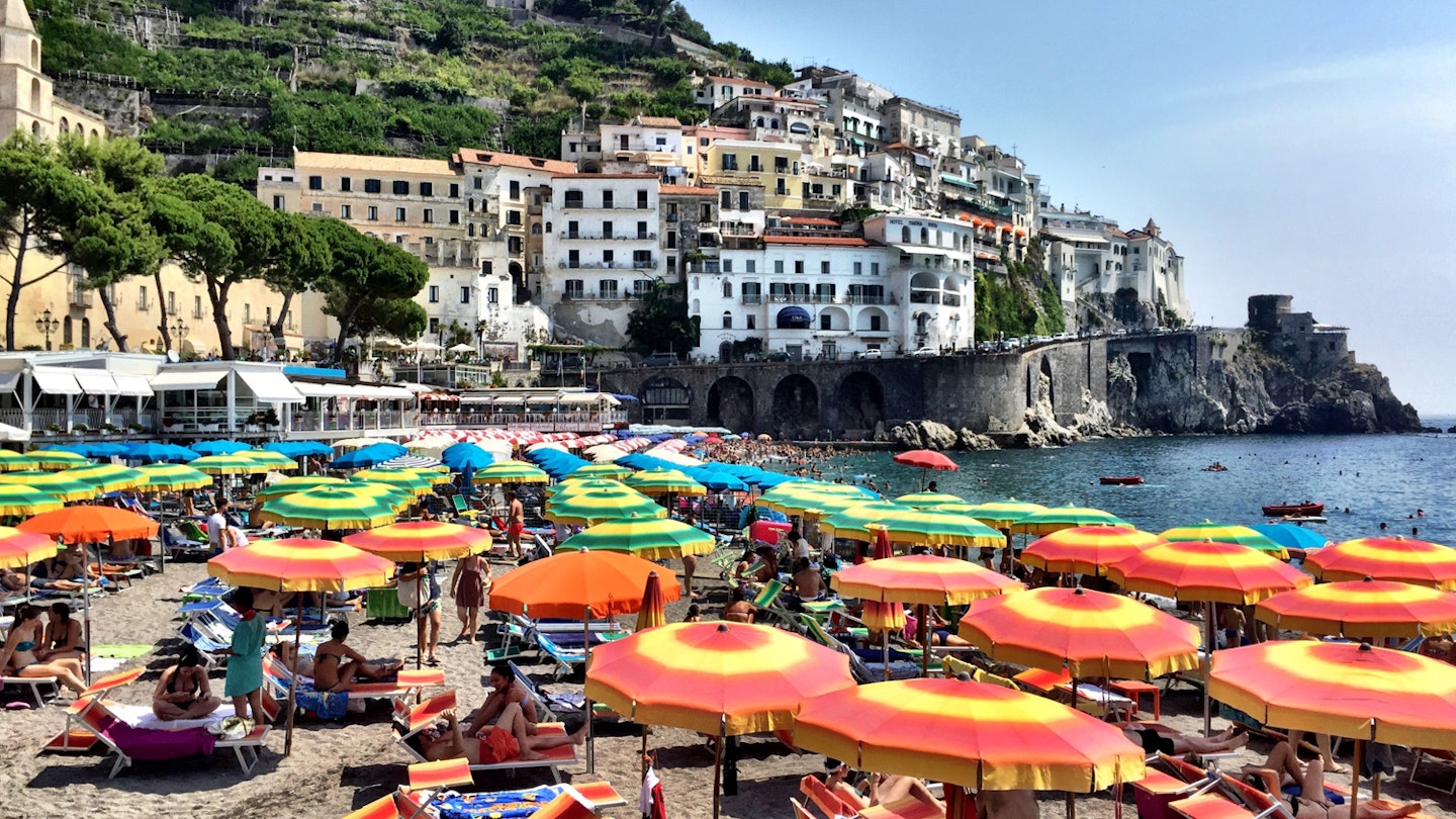 Beachgoers relaxing under umbrellas on the Amalfi Coast. Image by Mark Waind / EyeEm / Getty