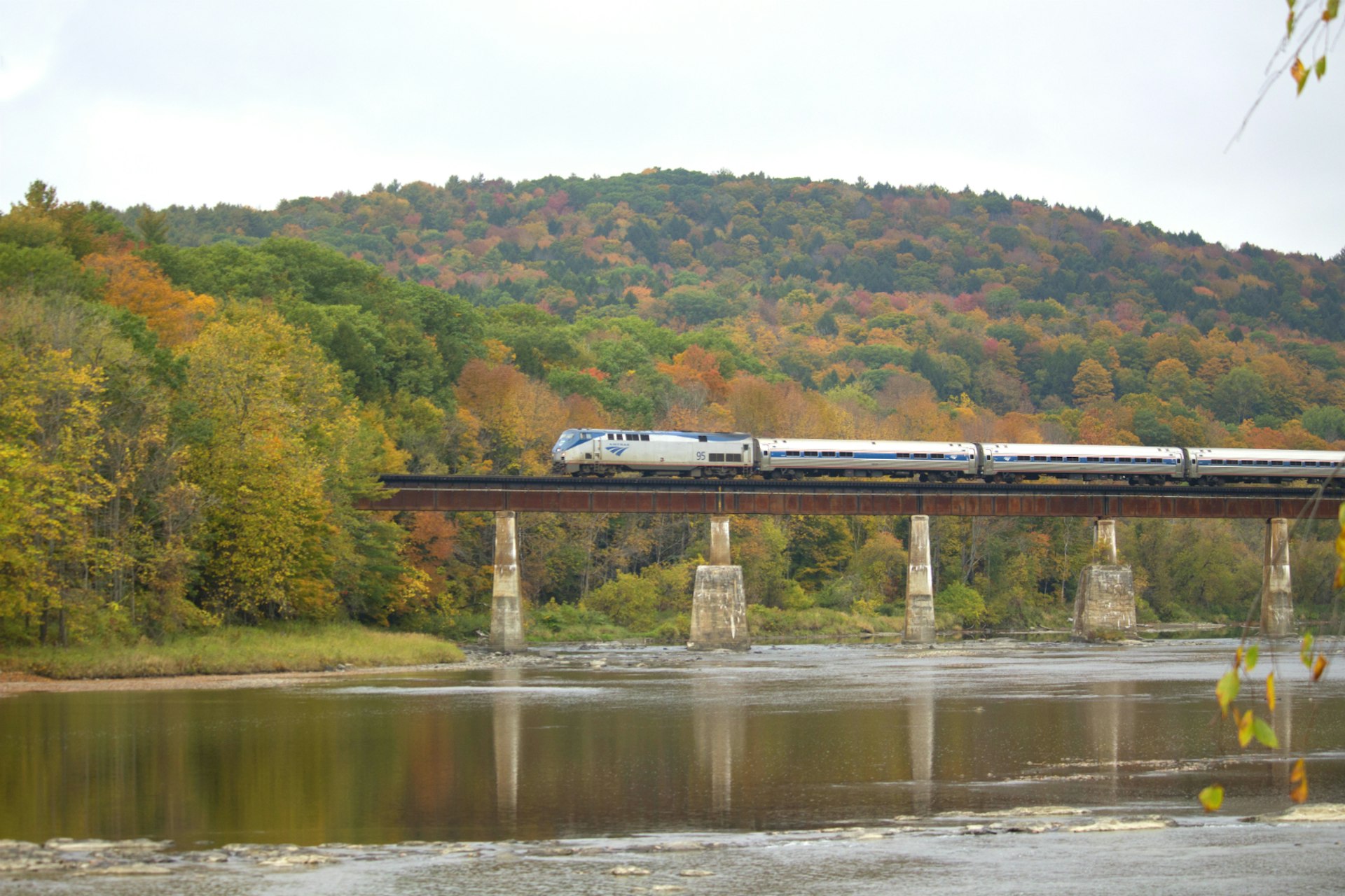 The Vermonter train traverses a bridge, with a backdrop of fall colours 