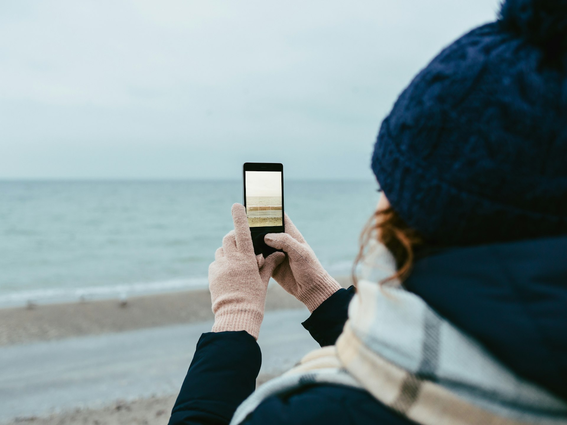 A woman taking a photograph of a beach on her smartphone