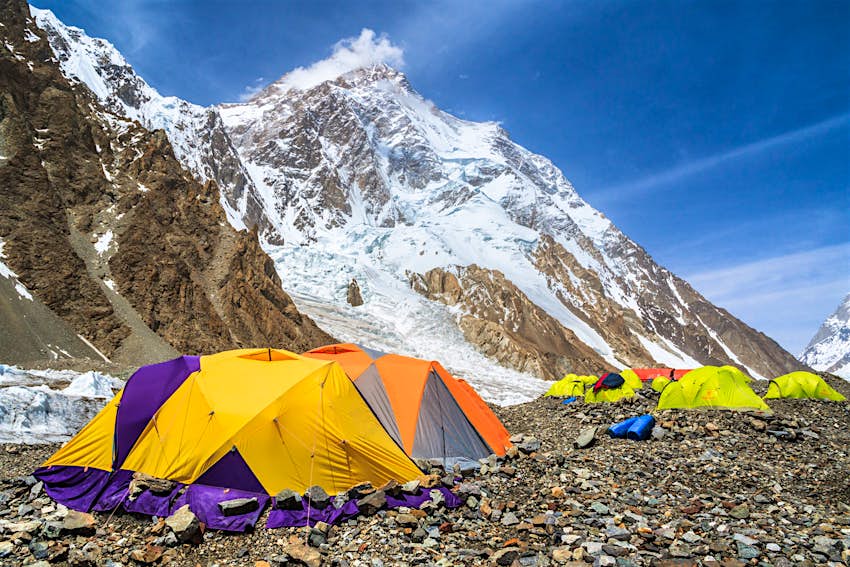 A number of colourful camping tents at K2 base camp. With the snowy summit standing in the background.