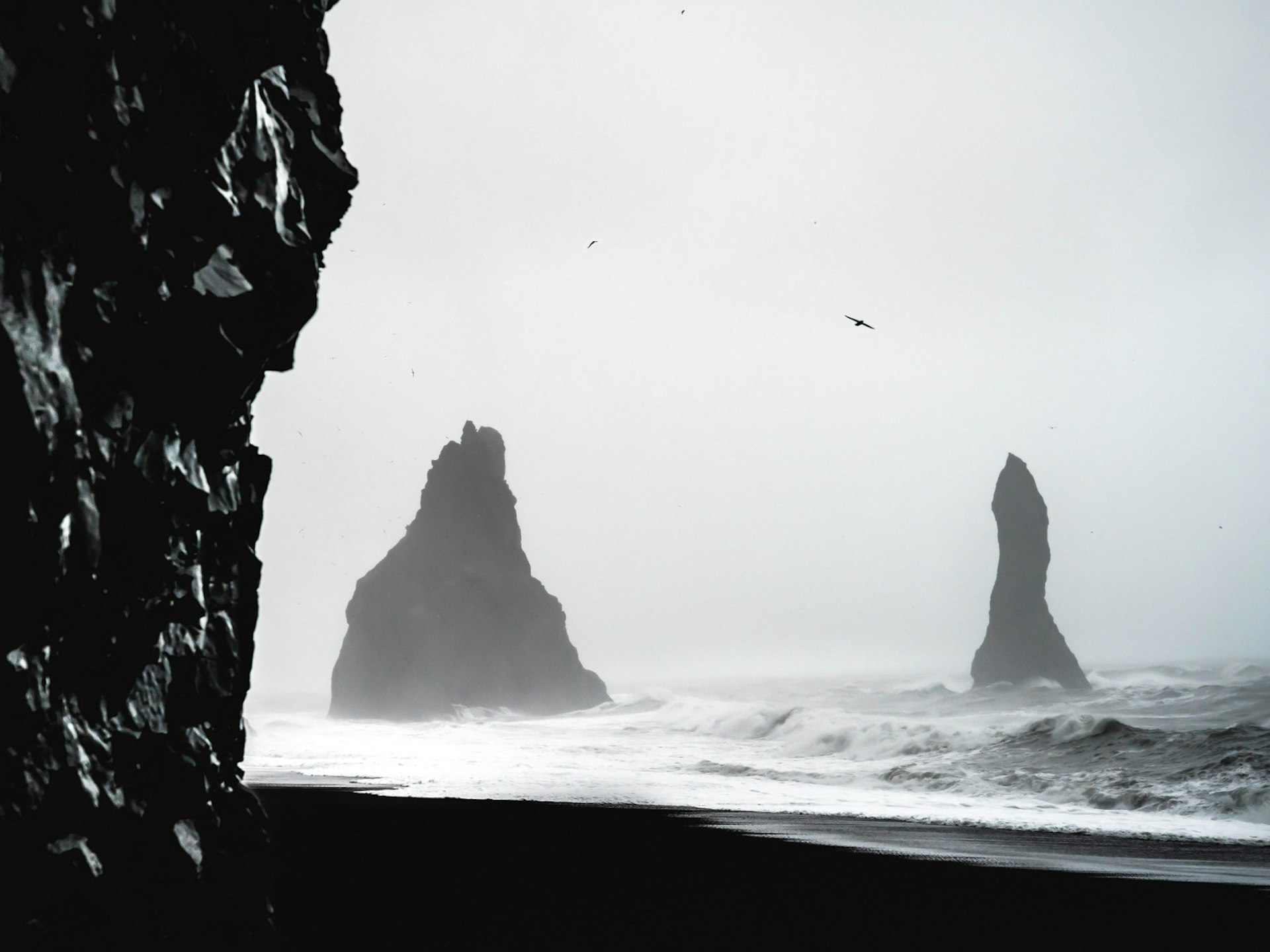 A black and white photograph of Reynisfjara Beach in Vik, Iceland.