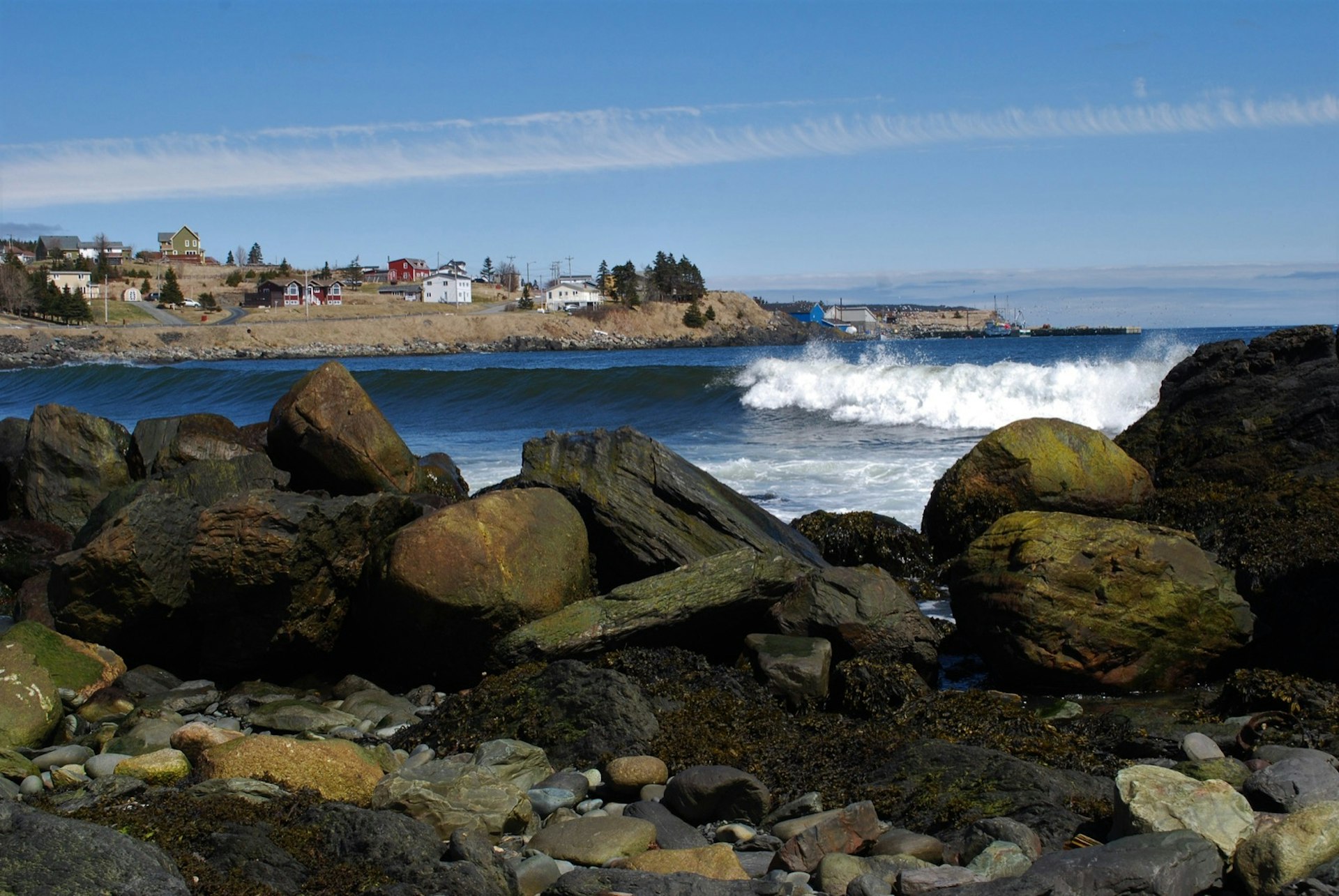 Wave rolling in to the beach, Witless Bay, Newfoundland. View from almost ground level looking across the beach to the water. Part of the town of Witless Bay can be seen in the background.