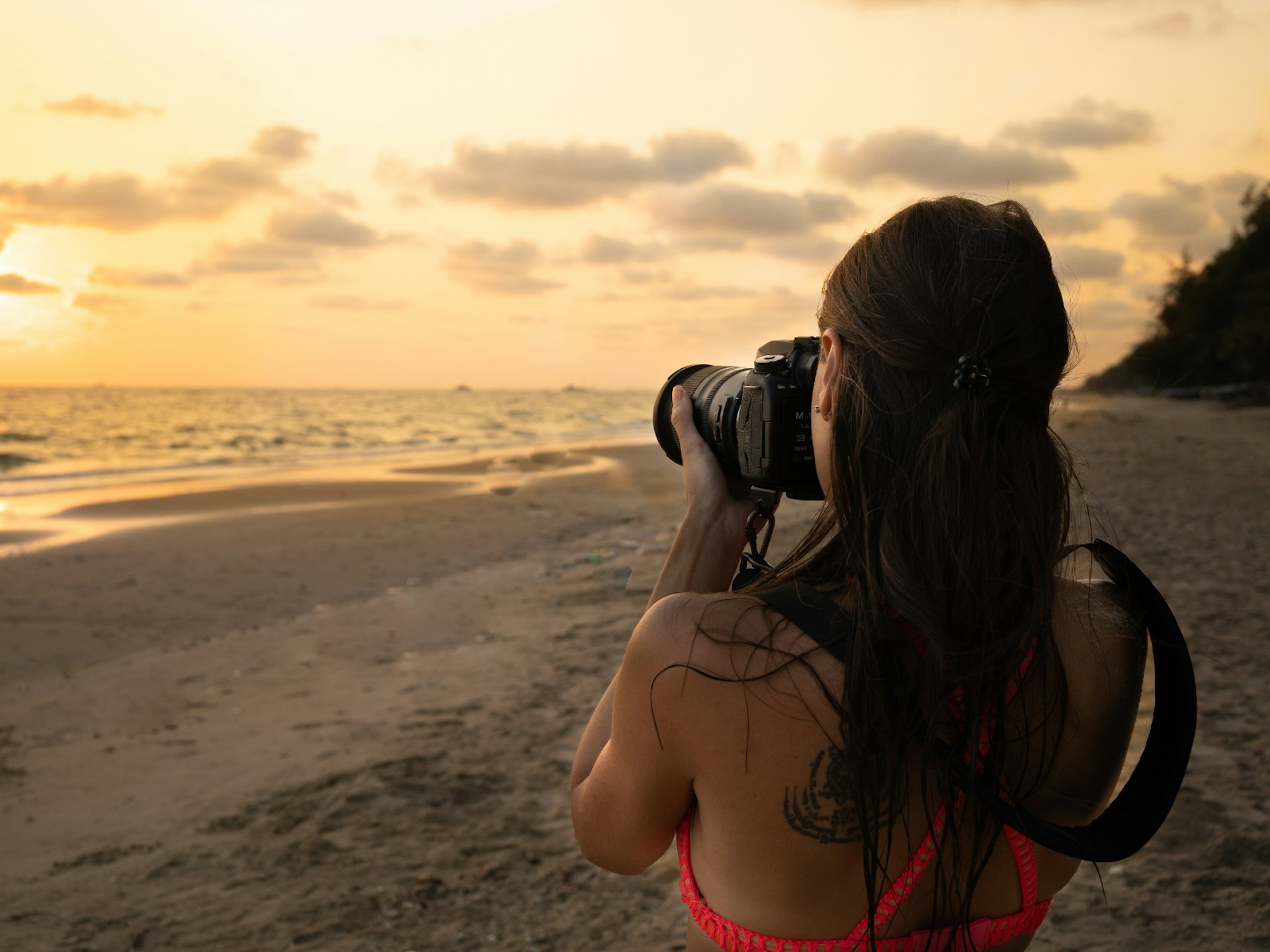 A woman photographing a beach at sunset