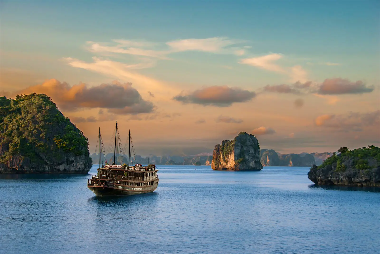 Features - Halong Bay A traditional boat sails on the waters of Halong Bay, with limestone pillars protruding from the water surrounding it
