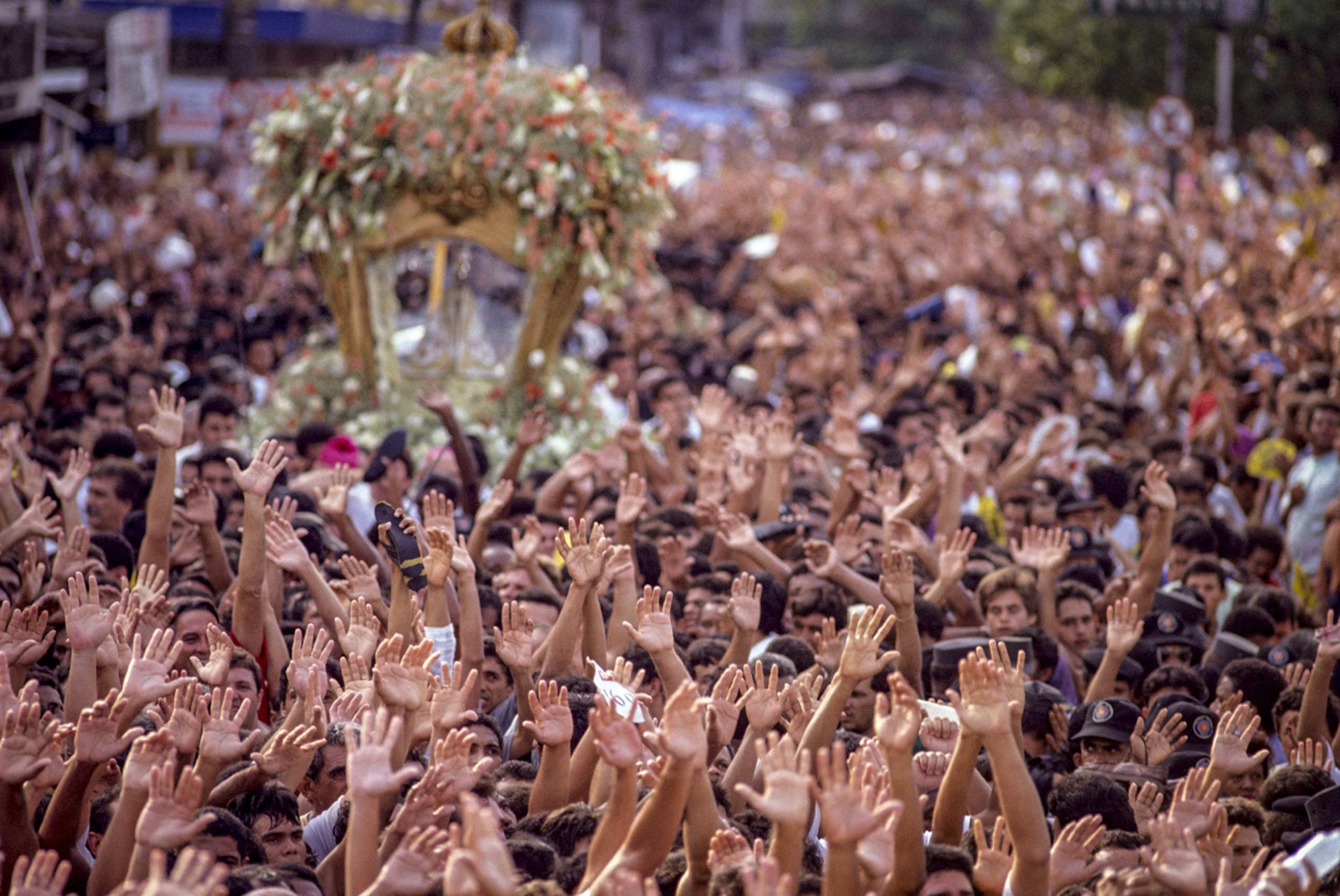 A dense crowd raises their hands to the air, with a religious altar in the background