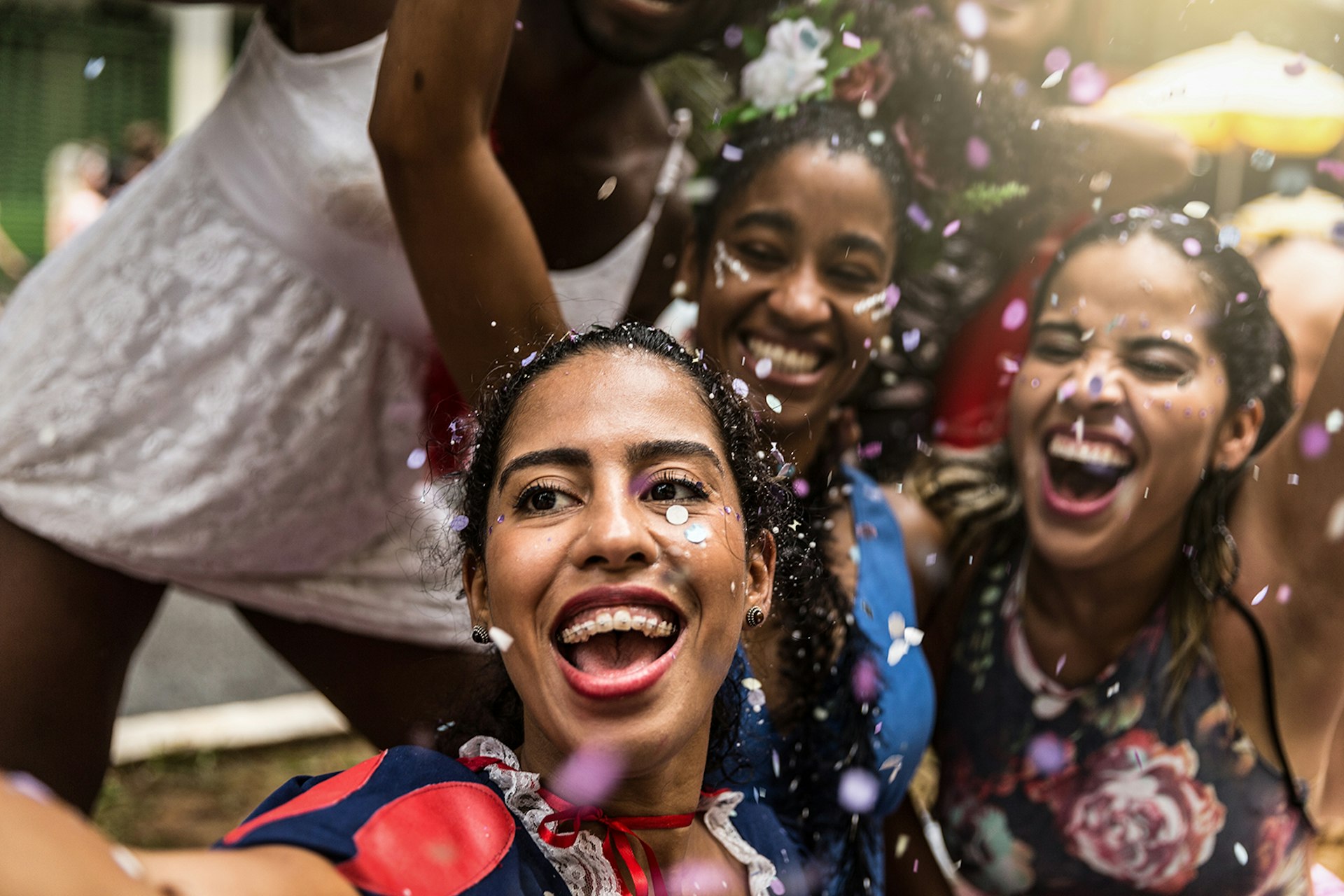 Four young women smile and cheer as confetti falls on them