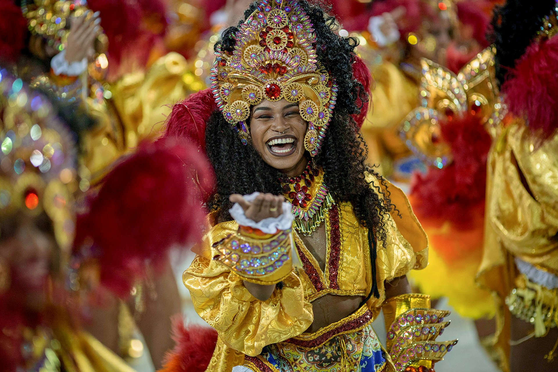 A woman dressed in a yellow and red Carnival costume blows a kiss at the camera