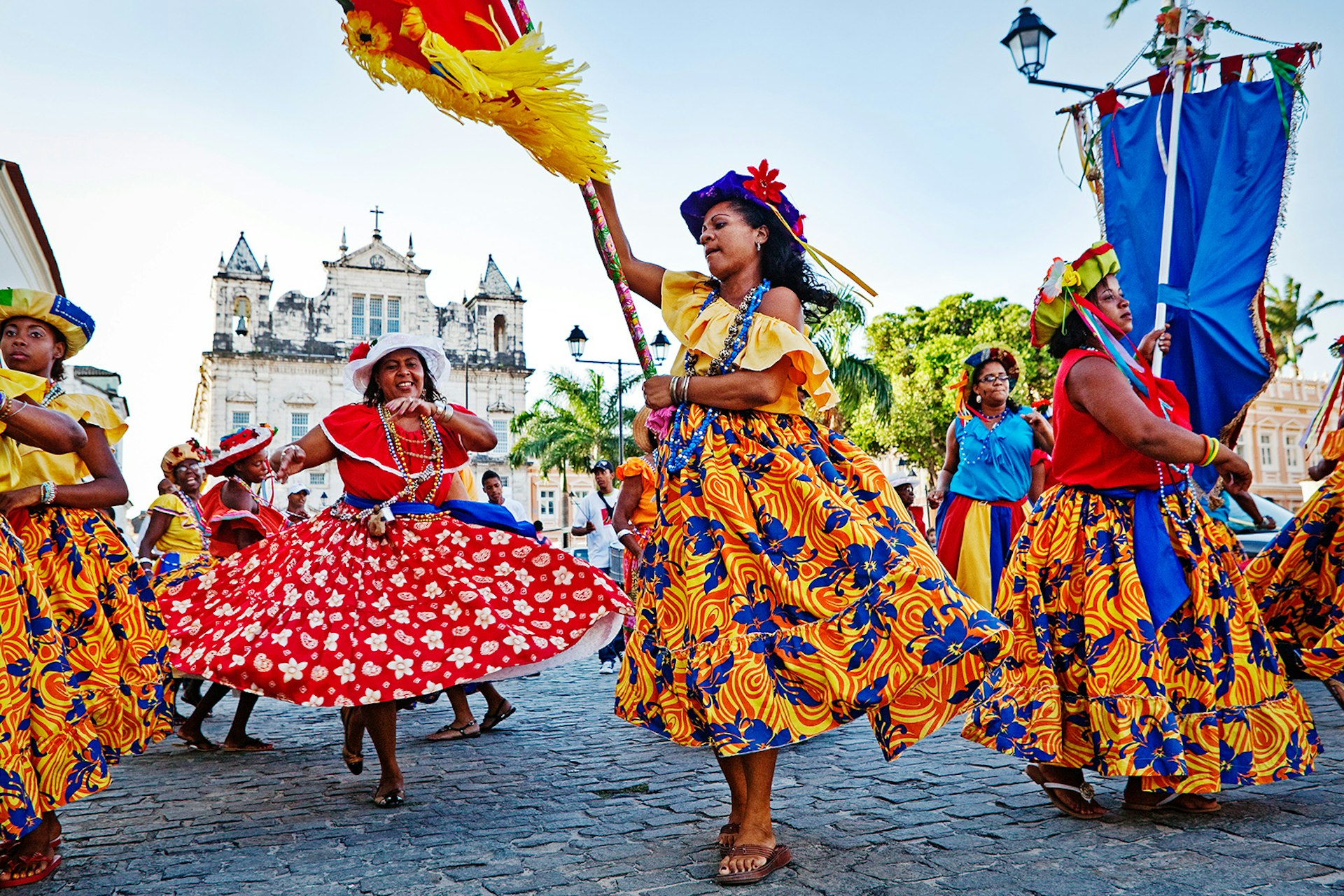 Women in colorful patterned skirts dance on a cobblestone street