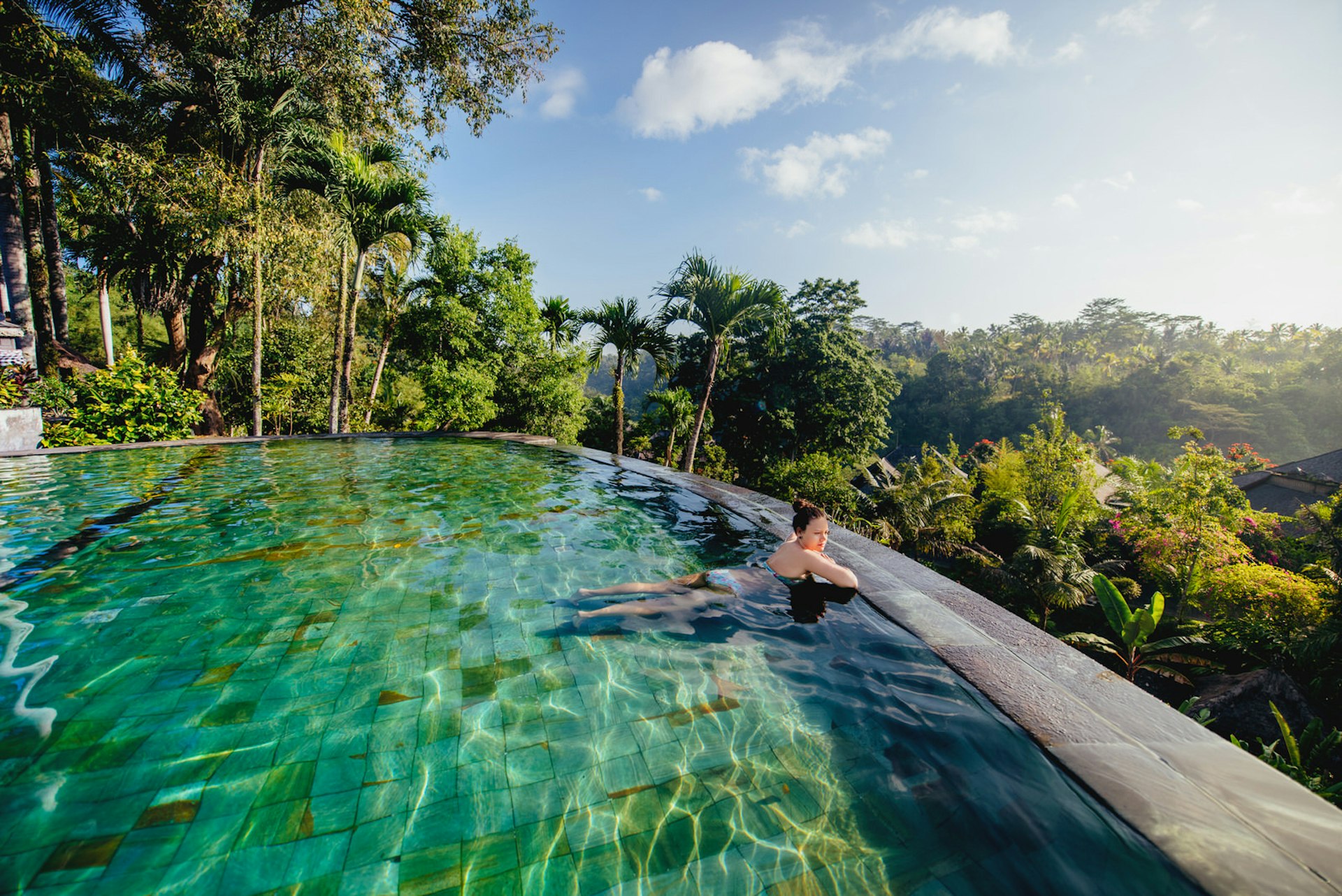A woman gazes across a lush valley from the edge of an infinity pool © bogdanhoda / Shutterstock 