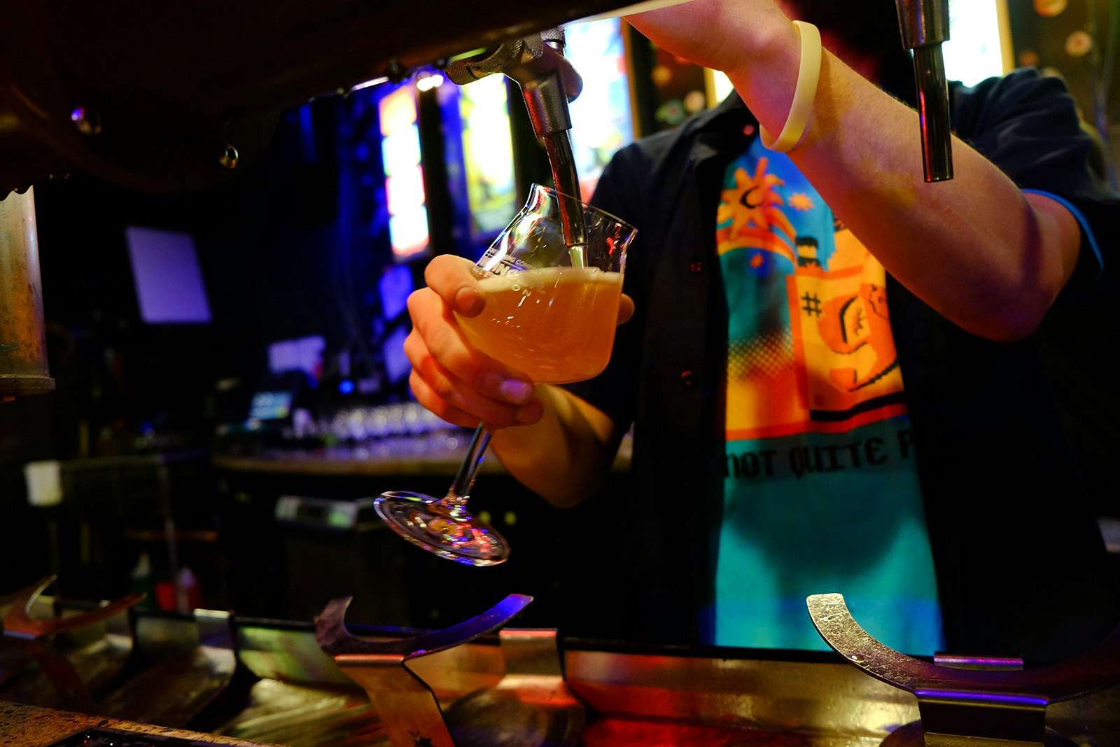 Close-up of man pouring beer into a tulip-shaped glass at a wooden bar at Magic Hat brewing. Many craft breweries in the states also have amazing food menus. 