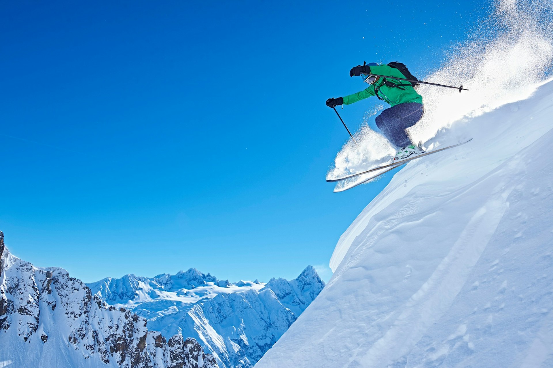 A skier launches into the air on the slopes of Chamonix, with snow-capped mountains beyond.