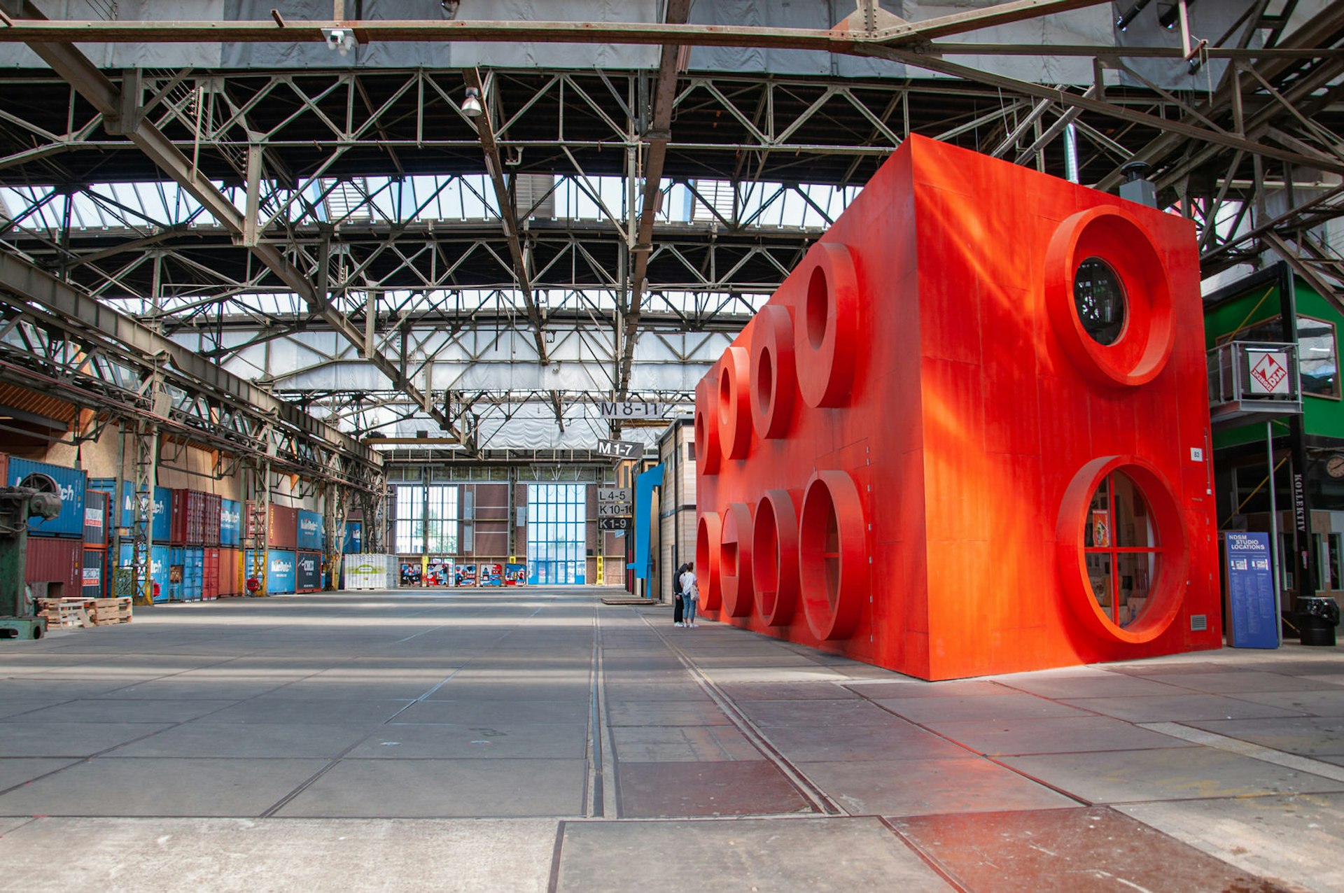 Interiören på ett av varven på Amsterdams NDSM-werf.  där en jättelik röd legokloss står utställd bland fraktcontainrarna