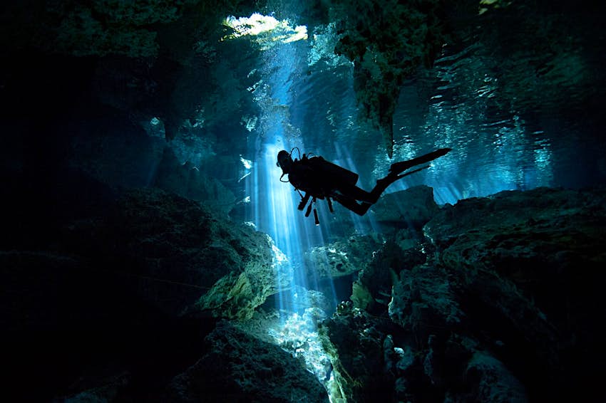 Features - GettyRF_141160759-d5101ffe1336 A scuba diver is silhouetted in front of a shaft of light as they explore a cenote (sinkhole) in Mexico
