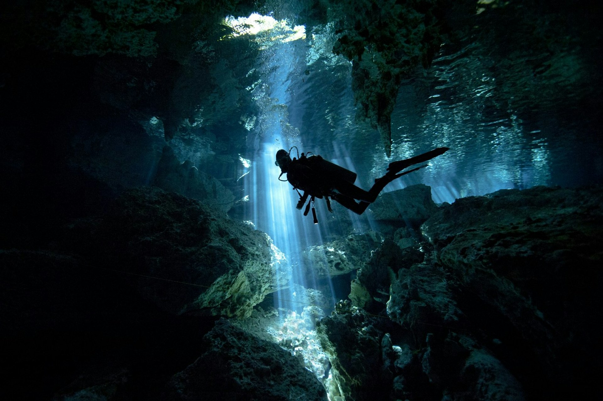 A scuba diver is silhouetted in front of a shaft of light as they explore a cenote (sinkhole) in Mexico