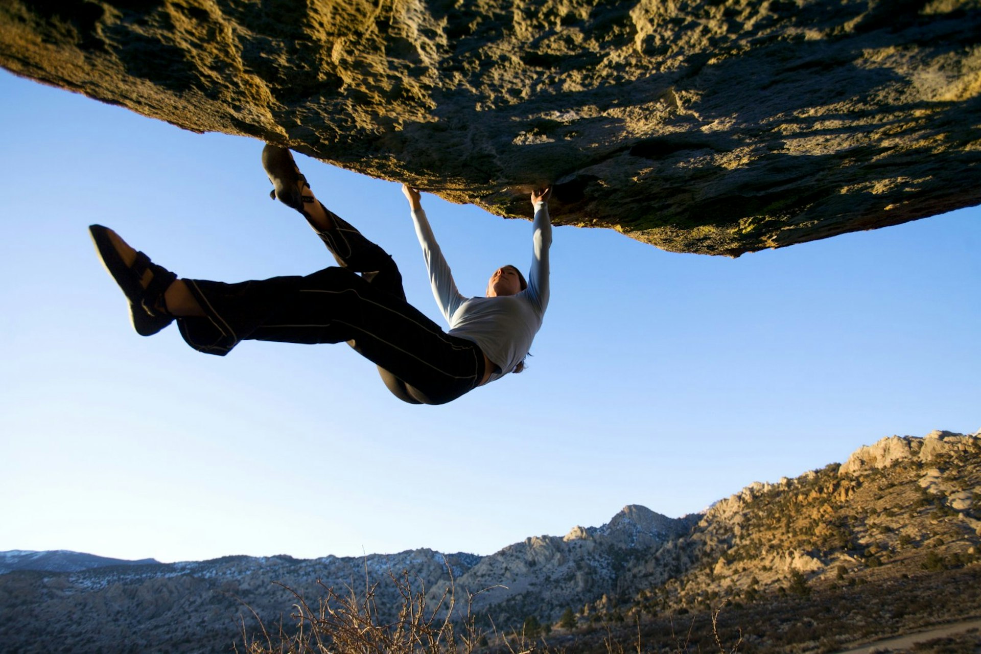 A woman, without equipment to support her, hangs below a rocky overhang