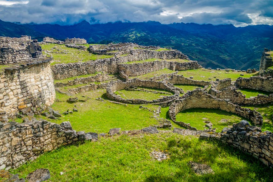 Peru travel - A view of the Kuelap citadel site, with a grassy field punctuated by foundations of stone walls and round homes