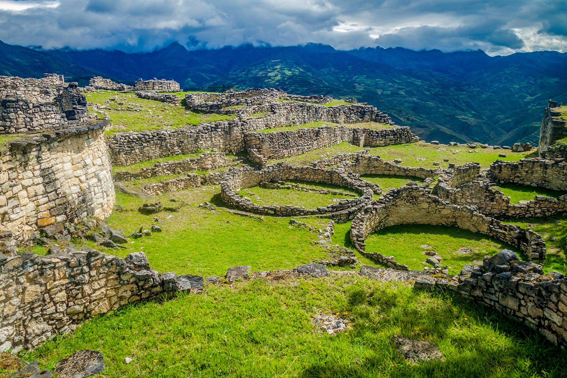 Peru travel - A view of the Kuelap citadel site, with a grassy field punctuated by foundations of stone walls and round homes