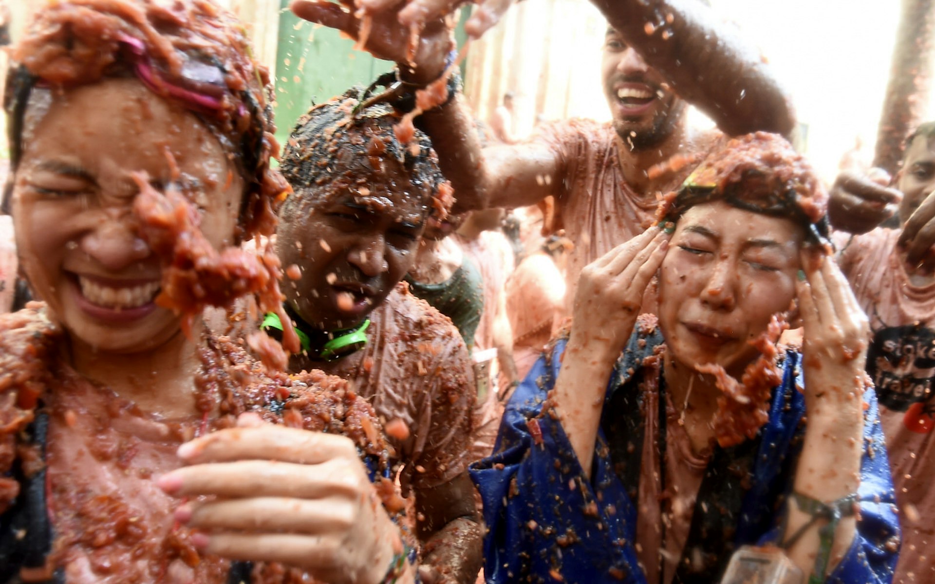 Revellers are covered with smashed tomato puree during the 'Tomatina' festival in Bunol. Everyone in the photo is being splattered with tomato pulp and squinting to try protect their eyes. It's pandemonium.