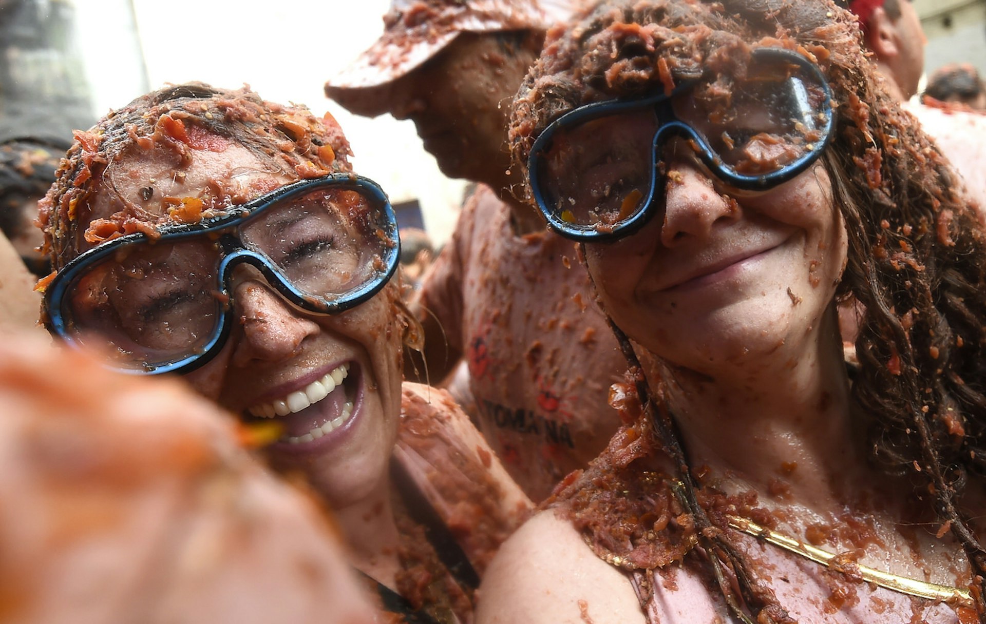 Two revellers sporting diving masks pose covered up with smashed tomatoes, during the 'Tomatina' festival in Bunol, on August 29, 2018. - This iconic annual fiesta that takes place on the last Wednesday of August and has been billed as "the world's biggest food fight". Two festival goers wear snorkelling goggles to protect their eyes from the tomato pulp