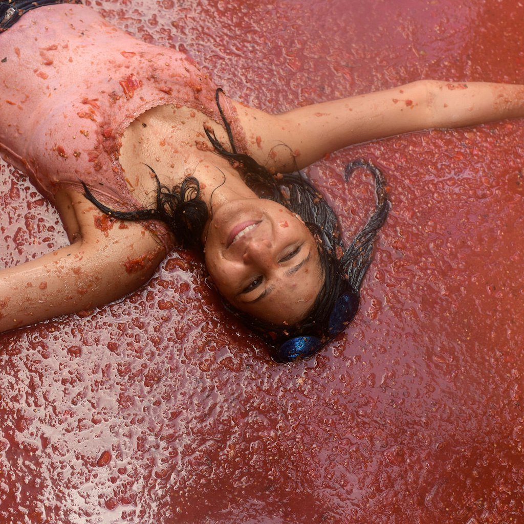 A reveller enjoys the atmosphere while participating in the annual Tomatina festival on August 29, 2018 in Bunol, Spain. The woman is lying on her back in a pool of tomato pulp, smiling with their eyes closed
