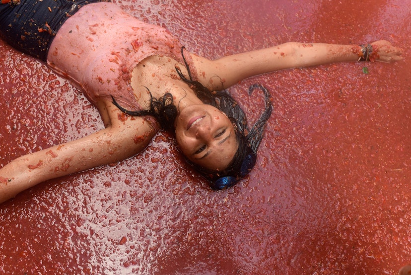 A reveller enjoys the atmosphere while participating in the annual Tomatina festival on August 29, 2018 in Bunol, Spain. The woman is lying on her back in a pool of tomato pulp, smiling with their eyes closed