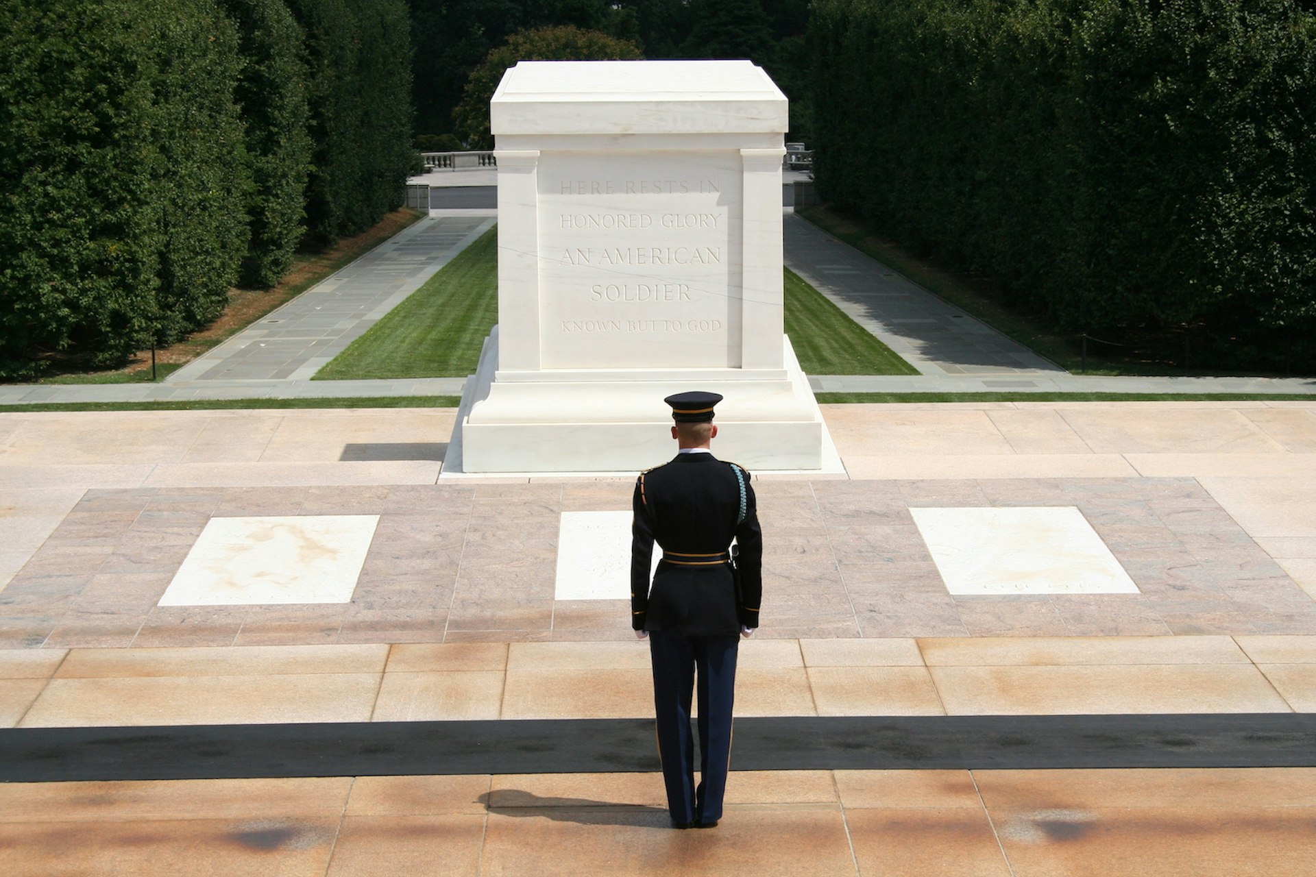 A soldier stands in front of the white marble tomb of the unknown soldier in Arlington National Cemetery on a sunny summer day; weekend in washington, DC