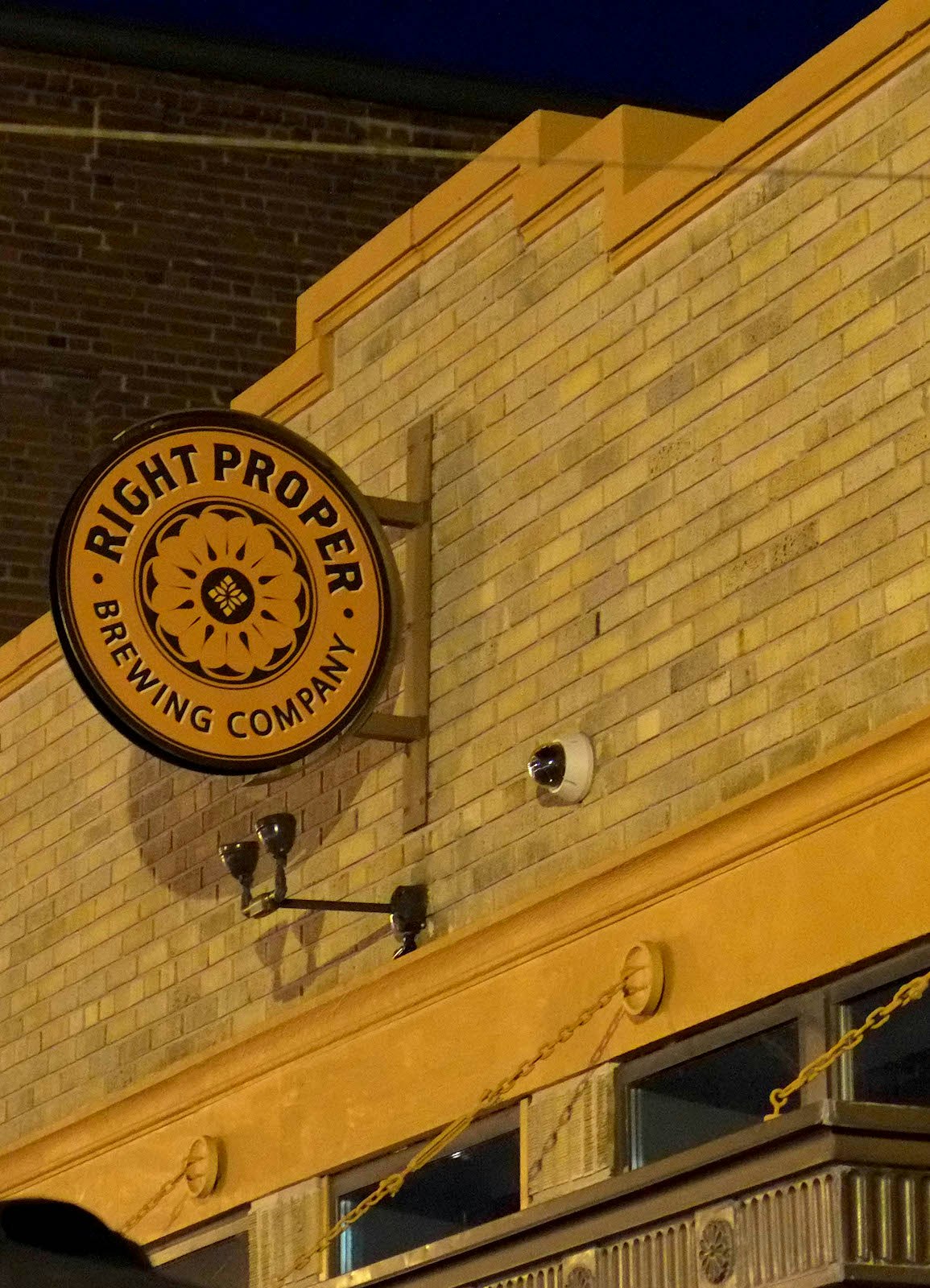 Exterior shot of a light brick brewpub with a circular yellow sign reading 'Right Proper Brewing'; weekend in washington, DC
