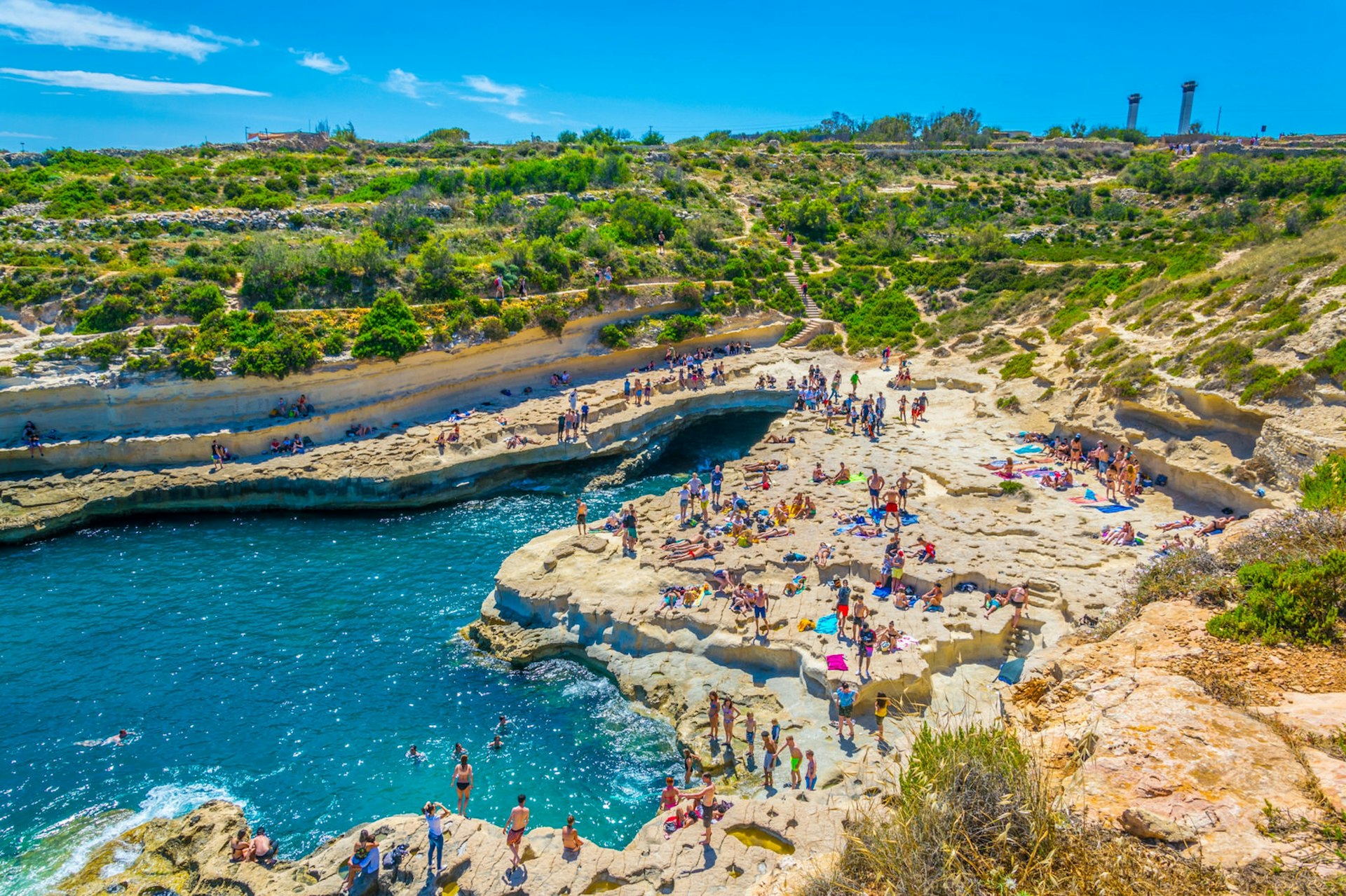 Groups of people relax on the rocks surrounding St Peter's Pool, a naturally formed sea pool