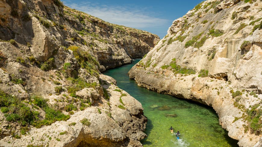 Wied il- Għasri in Malta is a narrow 'river' of sea water, running from the sea to a small sandy beach. In this image, two snorkellers swim through the narrow passage, with steep rock faces on either side of them 