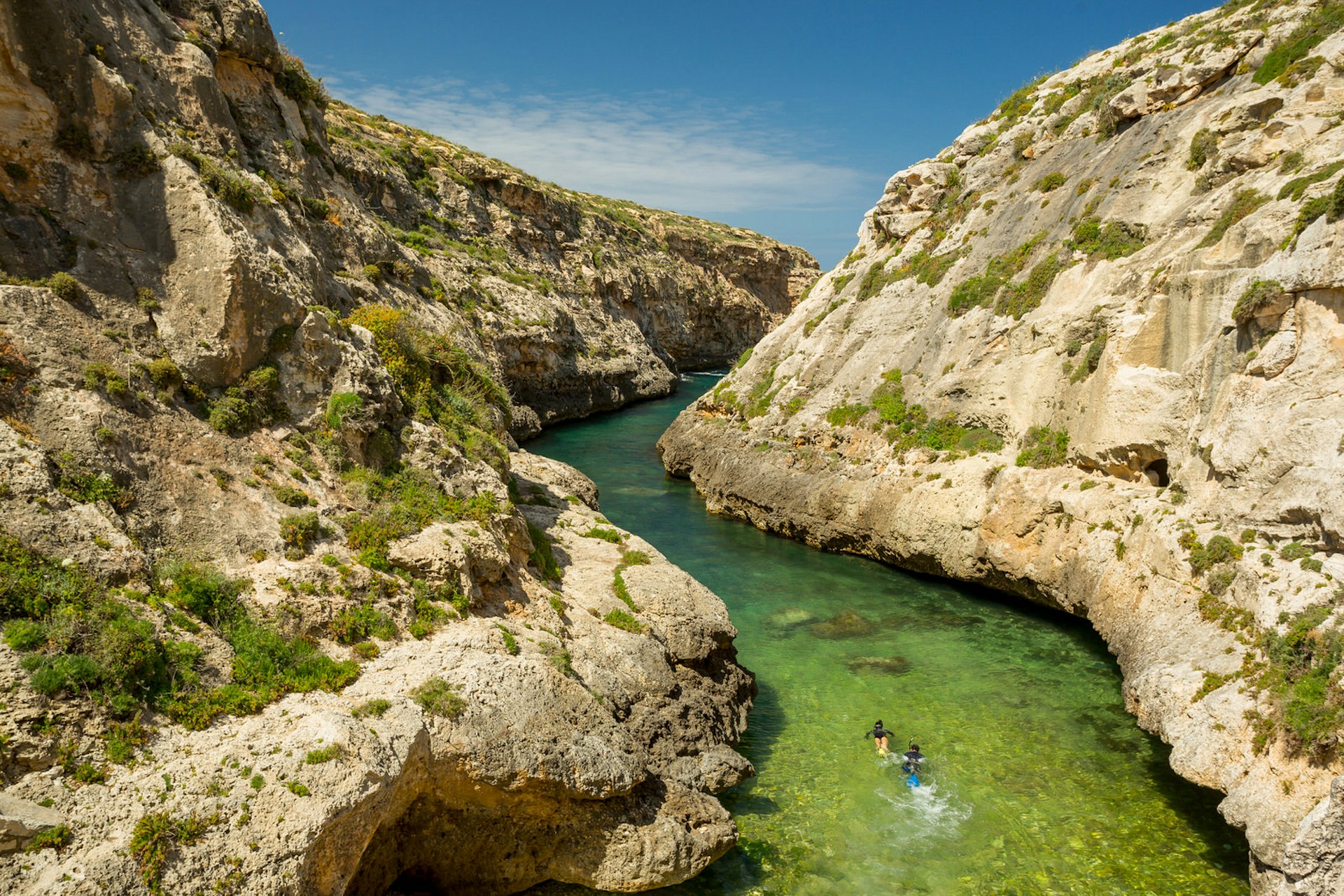 Wied il- Għasri in Malta is a narrow 'river' of sea water, running from the sea to a small sandy beach. In this image, two snorkellers swim through the narrow passage, with steep rock faces on either side of them 