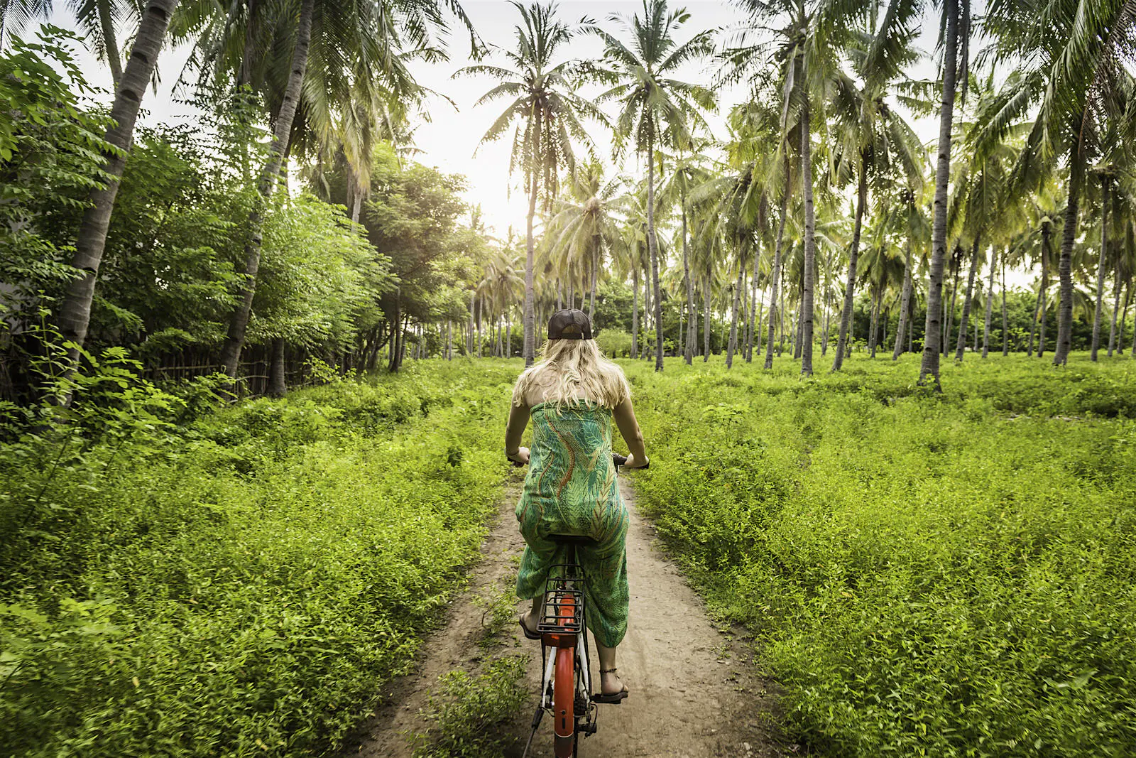 Features - Rear view of young woman cycling in palm tree forest, Gili Meno, Lombok, Indonesia The humble sarong: one minute it's a carefree fashion statement, the next it's a portable changing room © Manuel Sulzer / Getty Images