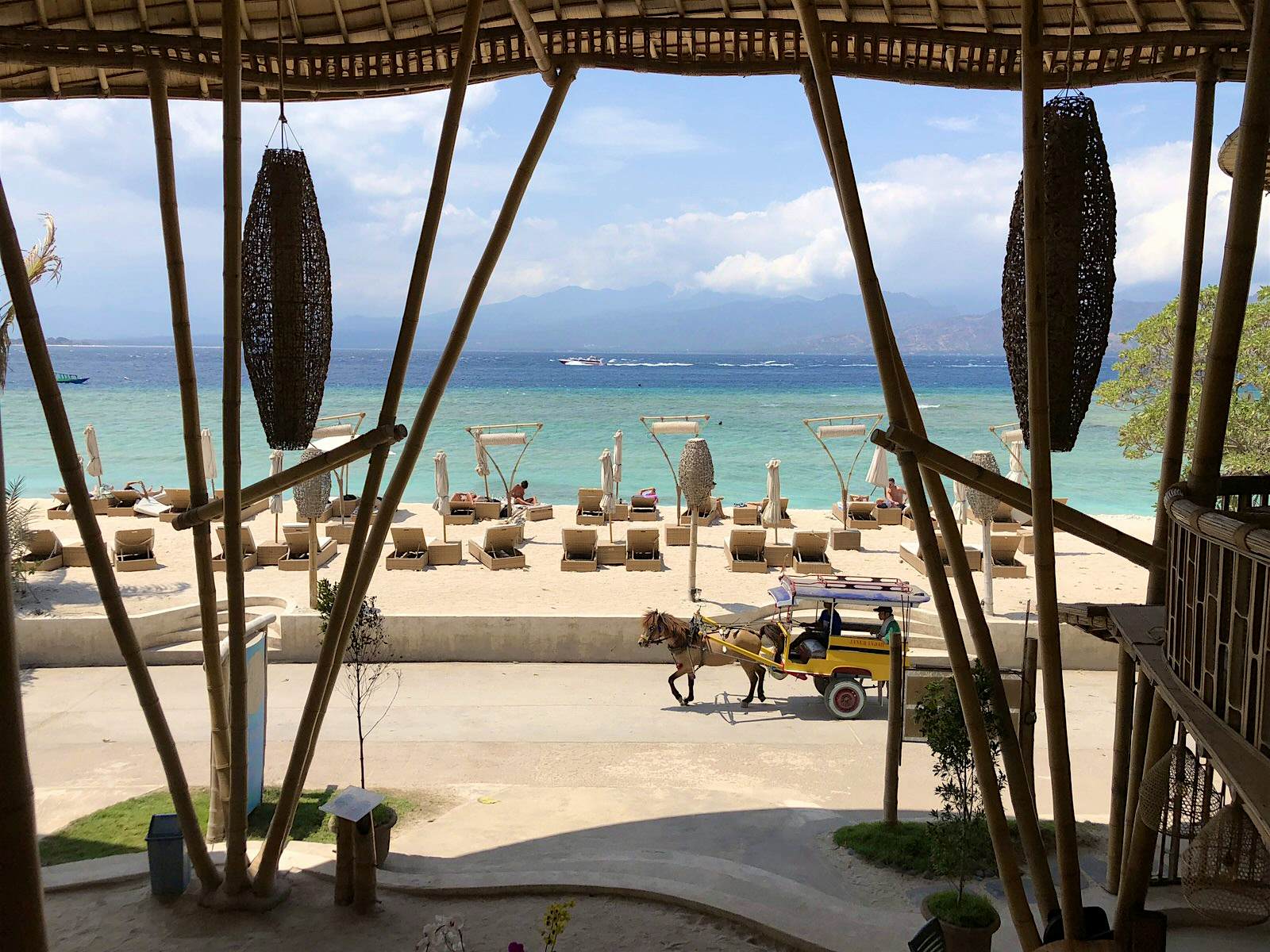 Gili Islands Gili T A yellow horse-drawn cart carries a passenger. The beach in the background has loungers and umbrellas in front of a beautiful sea