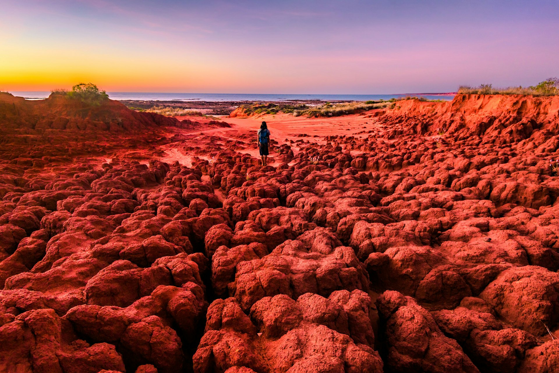 A woman looks out at the sunset from the red pindan soils of James Price Point at Dampier Peninsula. Western Australia