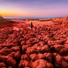A woman looks out at the sunset from the red pindan soils of James Price Point at Dampier Peninsula. Western Australia