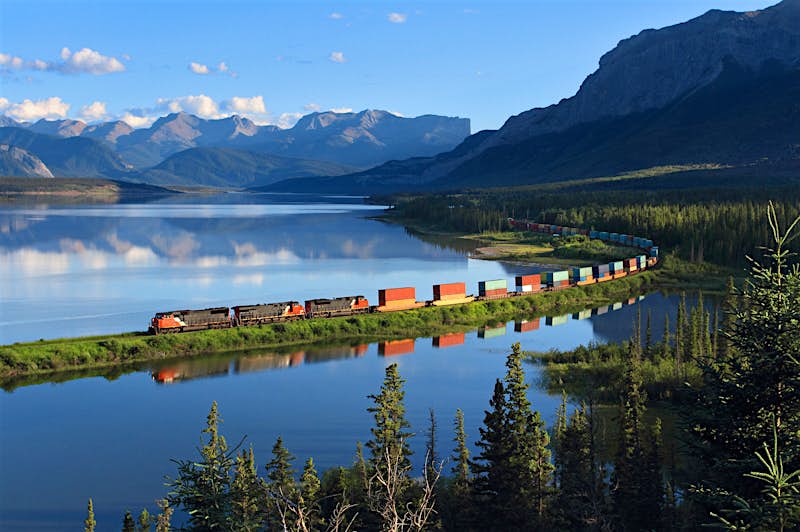 Features - Intermodal train curving by Brule Lake A freight train cruises through Swan Landing near Brule, Alberta; the train is reflected in the still waters of the lake while mountains are visible in the background