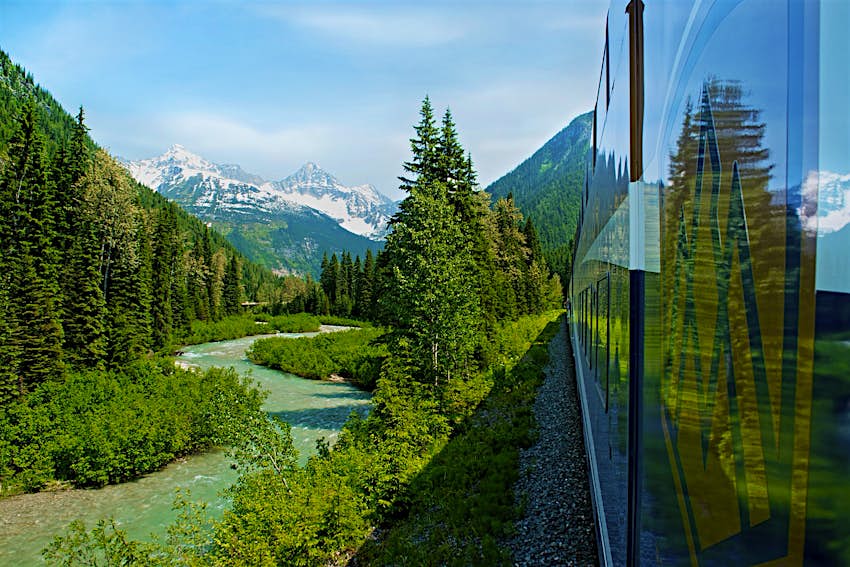 Image of a train passing through Canada's Banff National Park taken by a passenger out of a window; forests, rivers and mountains are visible