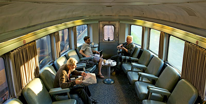 Features - Passengers awaiting departure on board The Canadian at Jasper railway station. The interior of the Canadian train, with several passengers sitting on comfortable, reclining chairs that line the walls
