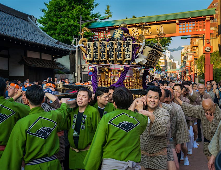 A large group of men in traditional outfits carry a mikoshi (portable shrine) through the street at the Sanja Matsuri